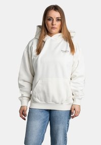 Hoodie bianco in pile con tasca a marsupio, polsini a costine e testo "PEGADOR" sul petto. Indossato con jeans blu.
