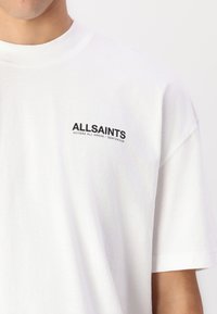 White cotton t-shirt featuring short sleeves, a crew neck, and a black text logo on the left chest reading "ALLSAINTS ACCESS ALL AREAS."