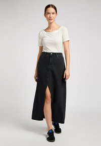 Jupe midi en denim noir avec fente devant, taille haute et cinq poches. Assortie à un haut léger en maille à manches courtes et des baskets noires.