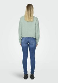 Pull cropped vert menthe avec coupe décontractée, ourlet et poignets côtelés, associé à un jean bleu ajusté et des chaussures noires épaisses, vu de dos.
