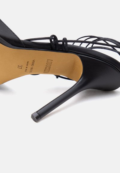Μαύρο σανδάλι με ψηλό τακούνι και λεπτά λουριά, με μυτερό τακούνι, που δείχνει την ταμπά εσωτερική σόλα όπου είναι χαραγμένο το όνομα της μάρκας και το μέγεθος 37.