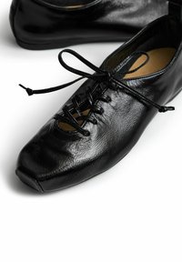 Scarpe in pelle nera con finitura lucida, dotate di un design stringato, punta rotonda e un dettaglio ritagliato sulla tomaia. Suola piatta.