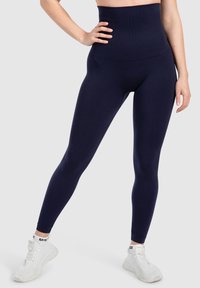 Leggings navy a vita alta in tessuto liscio ed elastico con un design aderente. Abbinati a scarpe da ginnastica bianche.