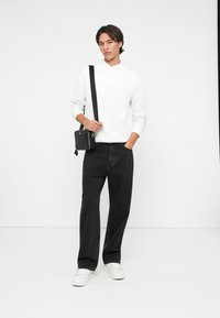 Bílý dlouhý rukáv top, černé široké džíny a bílé tenisky. Celkový vzhled doplňuje malá černá crossbody kabelka s odnímatelným popruhem.
