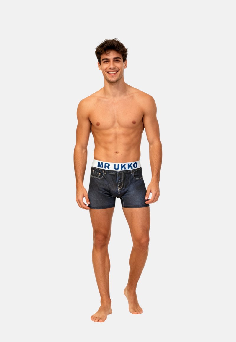 Mörk denimboxershorts med ett vitt elastiskt midjeband som har "MR UKKO" i blått. Modellen står barfota och poserar framifrån.