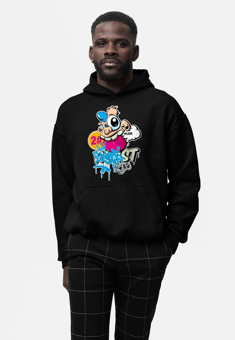 Mann trägt schwarzen Hoodie mit buntem Cartoon-Charakter und Graffiti-Design, kombiniert mit schwarz karierten Hosen, vor weißem Hintergrund stehend.