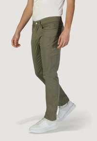 Pantalones ajustados verde oliva con bolsillos frontales, detalles de costura sutiles y cierre con cremallera, combinados con zapatillas blancas.