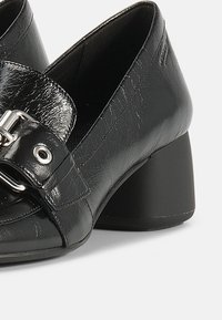 Czarne buty na obcasie z ekoskóry, zaokrąglonym noskiem, błyszczącym wykończeniem, akcentem w postaci klamry oraz grubym obcasem zapewniającym stabilność.