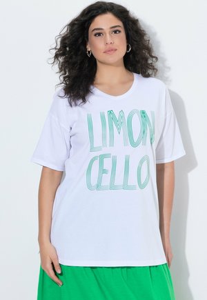 Frau mit lockigem Haar, die ein weißes T-Shirt mit grünem "LIMONCELLO"-Schriftzug und einen leuchtend grünen Rock trägt, steht vor einem weißen Hintergrund.