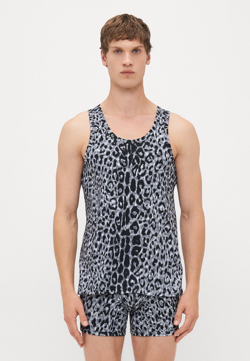 Junger Mann, der ein passendes Tanktop und Boxershorts im schwarzen und grauen Leopardenmuster trägt, steht vor einem schlichten weißen Hintergrund.