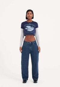 Maglietta grafica blu navy a maniche corte con design di onde; maniche lunghe azzurro chiaro; jeans larghi blu scuro; calzature nere; stile minimalista.