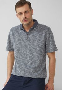 Koszulka polo w strukturalnym, niebiesko-szarym odcieniu, z kołnierzykiem, trzema guzikami i krótkimi rękawami. Noszona z ciemnymi szortami.