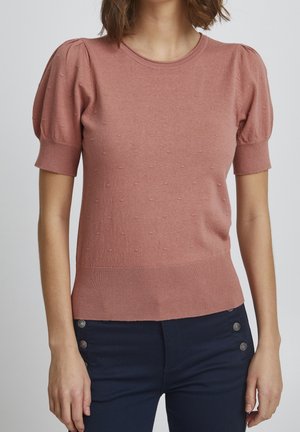 Woman wearing a dusty pink short-sleeve knit top with textured dots and navy pants with side button details.