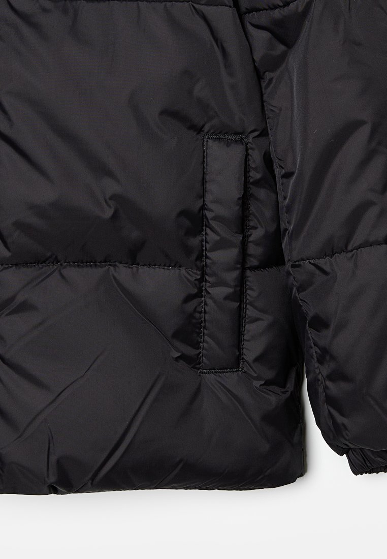 Schwarze Steppjacke mit gesteppten Abschnitten, einer Seitentasche und glatter, glänzender Textur. Das Material scheint leicht und wasserabweisend zu sein.