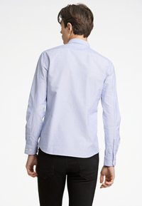 Camicia a righe in blu chiaro e bianco, realizzata in cotone, con maniche lunghe e orlo curvo con polsini abbottonati.