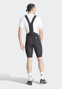 Pantaloni da ciclismo neri con salopette e maglietta bianca a maniche corte, dotati di bretelle elastiche, sella imbottita e loghi del marchio sui capi.