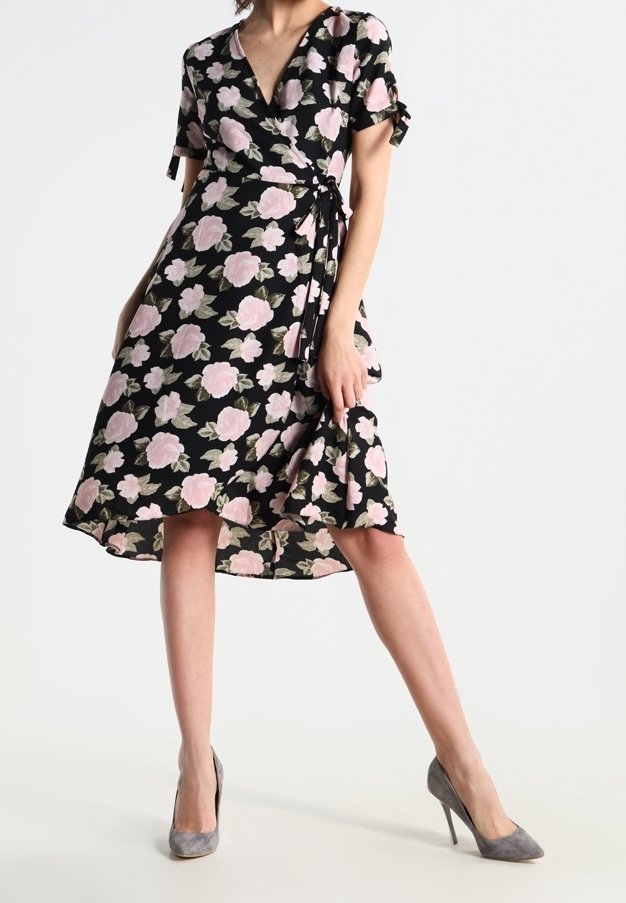 Schwarzes Wickelkleid mit pinken Blumenmuster, kurzen Ärmeln und Rüschensaum, aus leichtem Stoff. Kombiniert mit grauen High Heels.