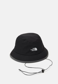 Cappello a secchiello nero realizzato in tessuto impermeabile con una visiera ampia. Presenta un cordino e un dettaglio con logo argentato sul lato.