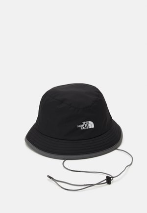 Cappello a secchiello nero realizzato in tessuto impermeabile con una visiera ampia. Presenta un cordino e un dettaglio con logo argentato sul lato.