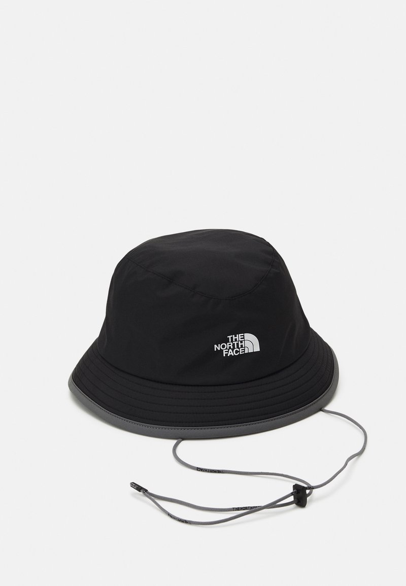 Cappello a secchiello nero realizzato in tessuto impermeabile con una visiera ampia. Presenta un cordino e un dettaglio con logo argentato sul lato.