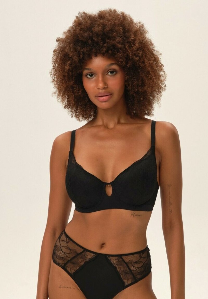 Czarny biustonosz z koronkowymi detalami i fiszbinami, z kluczowym wycięciem na środku. Pasujące czarne koronkowe figi z półprzezroczystymi akcentami.