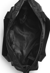 Svart nylon duffelväska med dragkedjestängning. Inuti har den en slät satininsida, flera fack och en mjuk textur.