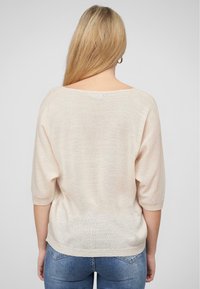 Helles rosa, gestricktes Sweatshirt mit weitem Ausschnitt und kurzen Ärmeln. Hat eine weiche Textur und eine lockere Passform, kombiniert mit blauen Jeans.
