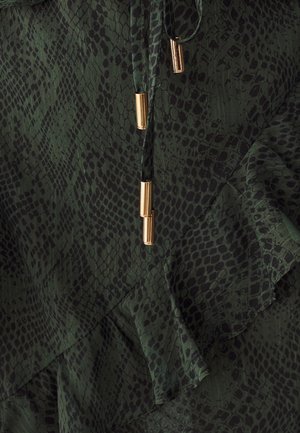 Groen slangenprintstof met een gerimpelde rand en gouden hardware-accenten op een trekkoorddetail, dat textuur en patroon benadrukt.