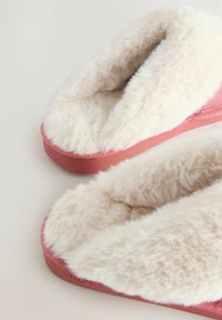 Faux fur slippers with a light cream interior and a pink textured exterior. Rounded shape with a cushioned footbed for comfort.