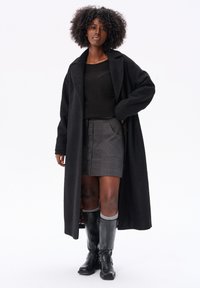 Czarny długi płaszcz z teksturowanej tkaniny, w połączeniu z szaro-skalanym spódnicą w kratę z guzikami oraz czarnymi kozakami do kolan z klamerkami.
