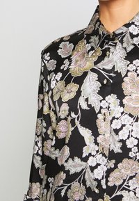 Camicia nera a fiori con grandi e vivaci fiori rosa e verdi, colletto con bottoni e bottoni lucidi, realizzata in tessuto morbido.