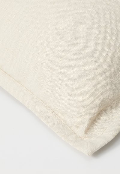 Square cushion in textured cream fabric with a visible seam detail and soft finish, designed for comfort and understated elegance.