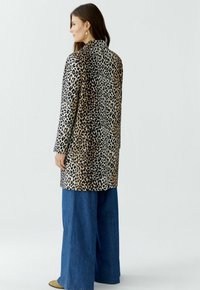 Leopardenmuster mantel mit maßgeschneidertem Design, ausgestattet mit einem schwarz-braunen Farbschema, langen Ärmeln und einem geraden Schnitt hinten. Kombiniert mit weit geschnittenen Jeans.