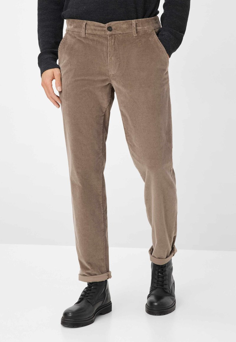 Corduroy broek in lichtbruin met een verticale ribbeltextuur, voorzien van een knoop en zakken, gecombineerd met zwarte veterschoenen.