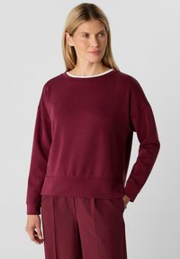 Bordeaux sweatshirt met een ronde hals, lange mouwen, geribde manchetten en een licht gestructureerde stof; heeft een klein logo aan de onderkant.