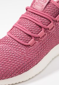 Rosa stickad sneaker med texturerat tyg, matchande snörning och varumärke på tungan. Har en vit gummisula och vadderad krage.