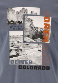 Grå t-shirt med svartvita fotografier av landskap, med orange och svart text som står "ADRENALIN, DENVER, COLORADO."