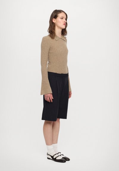 Beige ribbet genser med krage, kombinert med knelange marineblå stripete shorts. Sorte sko med hvite detaljer.