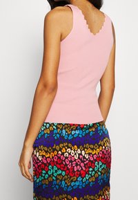 Canotta a coste rosa con scollatura smerlata, abbinata a una gonna multicolore con stampa leopardata con tonalità blu, rosse e dorate.