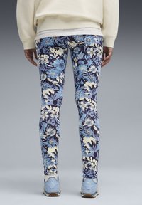 Bloemleggings met een donkerblauwe achtergrond, versierd met blauwe en crèmekleurige bloemen, gemaakt van rekbaar materiaal en met een aansluitende pasvorm. Draagt bij lichte blauwe sneakers.