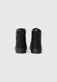 Botas de tobillo negras con material sintético suave, puntera redondeada, cuello acolchado y suela de goma texturizada. Diseño simple y elegante.