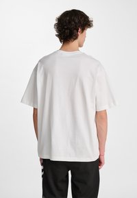 Biały bawełniany T-shirt o luźnym kroju, z krótkimi rękawami i klasycznym okrągłym dekoltem; gładka faktura, prosty design, brak widocznych wzorów lub logo.