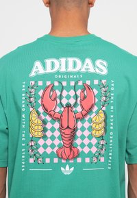 Zöld pamut póló, nagy rózsaszín homárral, citromszeletekkel és kockás háttérmintával, "Adidas Originals" felirattal.