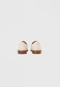 Flødefarvede lædersko med en glat finish, der har en rundet tå og en kontrasterende brun træhæl.