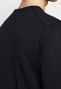 Ciemnogranatowy sweter o gładkiej teksturze, z okrągłym dekoltem i szwami na ramionach. Tkanina wydaje się miękka i lekka.