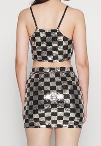 Completo composto da top corto e mini gonna in paillettes nere e argento, caratterizzato da un motivo a scacchi, spalline sottili e una vestibilità aderente.