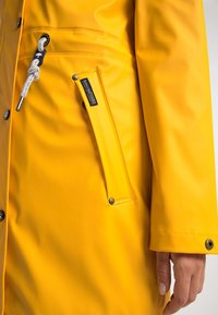 Žlutý voděodoln�ý deštník s hladkým povrchem, nastavitelnou kapucí s šňůrkou a boční kapsou. Obsahuje patentky a kontrastní stehy.