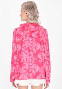 Felpa rosa floreale con maniche lunghe, caratterizzata da un motivo di ibisco e foglie di palma, e un cappuccio regolabile. Tessuto morbido e leggero.