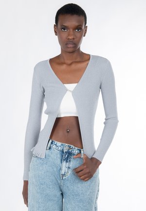 Cardigan grigio a coste con scollo a V e dettaglio di chiusura frontale, abbinato a pantaloncini di jeans a vita alta color azzurro chiaro. Texture liscia e design aderente.