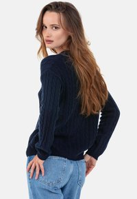 Pull en maille torsadée bleu marine à manches longues, avec poignets et ourlet côtelés. Porté avec un jean bleu clair, coupe décontractée.